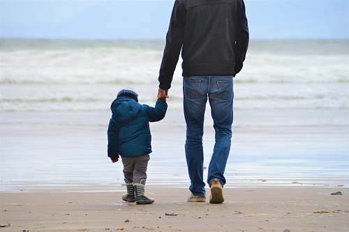 holding hands man and boy walking on seashore under blue sky person